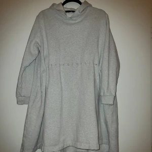 Ljusgrå hoodieklänning - Säljer en mysig grå hoodieklänning med långa ärmar och huva. Klänningen har en avslappnad passform och dekorativa sömmar i midjan. Perfekt för en bekväm och stilren look. Något längre bak. 