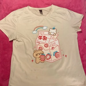 Beige t-shirt med sött tryck - Säljer en ljusgul t-shirt med ett gulligt tryck av björnar och jordgubbar. T-shirten har korta ärmar och en rund halsringning.🍓🐻