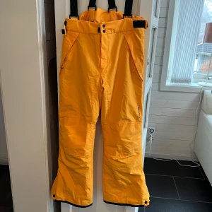 Orange skidbyxor från Everest - Säljer ett par orange skidbyxor från Everest. De har justerbara hängslen och knäppning i midjan. Perfekta för vinterns kalla dagar med sin varma och skyddande design.