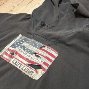 Grå hoodie från Ralph Lauren - Säljer en grå hoodie från Ralph Lauren med en stor amerikansk flagga på framsidan.