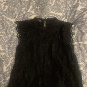 Svart spetsblus från Pieces - Säljer en elegant svart spetsblus från Pieces. Blusen är ärmlös med fina spetsdetaljer vid axlarna och halsen. Perfekt för en stilren look. Storlek XS!💕 Skriv vid mer bilder eller info!