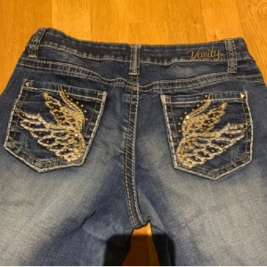 Blå jeans med fina strass fickor - Snygga blå jeans från Vanity med unika broderade vingar på bakfickorna. De liknar miss me jeans, är i jättebra skick men är lite för små på mig och det är av den andledningen jag säljer dem. Innerbens längden är 73cm och midje måttet är 78 cm