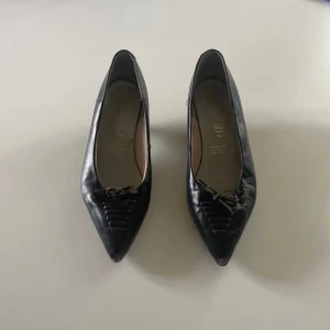 Kitten heel spetsig tå  -  Svarta kitten heels  med spetsig tå och liten klack. Skorna har en dekorativ detalj framtill och är tillverkade i skinn. Köpa vintage och använda. Står ingen storlek men uppskattar 36.5. 