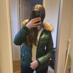 Grön vinterjacka med äkta päls och bälte - En snygg, lyxig och unik grön jacka med äkta päls på huvan. Jackan har dragkedja och ett bälte (avtagbar) i midjan för en figurnära passform. Perfekt för kyliga dagar. 