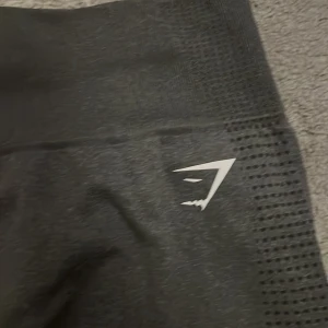 Svarta leggings från Gymshark - Säljer ett par svarta leggings från Gymshark i storlek M. De är perfekta för träning med sin tighta passform och höga midja. Materialet är stretchigt och bekvämt, vilket gör dem idealiska för gymmet eller yoga. De har en diskret logga på sidan och ett mönster som ger extra stil.