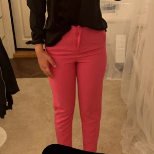 Rosa byxor - Säljer ett par snygga rosa byxor i normal passform. De är perfekta för att liva upp garderoben och funkar både till vardags och fest. Byxorna har en enkel design med dragkedja och knappar framtill. De är i mycket bra skick och redo för en ny ägare!