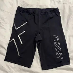 Säljer ett par svarta träningsshorts från 2XU i mycket bra skick. Strl M.De är tillverkade i ett stretchigt material med elastisk midja för bästa passform. Perfekta för träning och har snygga silverfärgade detaljer på sidorna. Passar perfekt för både gym och löpning!