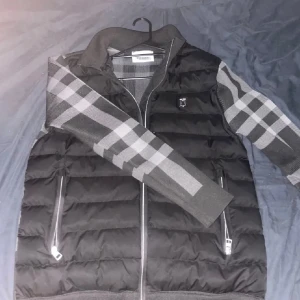 Burberry cardigan - Säljer en snygg svart och grå cardigan från Burberry. Cardiganen har en quiltad design med dragkedja och långa ärmar. Perfekt för höst,vinter och vår med sin stilrena look och varma material. Passar både till vardags och fest! Pris kan såklart diskuteras!