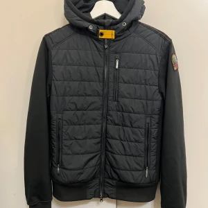  Parajumpers Jacka - Säljer en svart fleece och pufferjacka från Parajumpers i storlek XS. Jackan har en quiltad design med dragkedja och en praktisk huva. Perfekt för kyliga dagar med sin kombination av stil och funktionalitet. Märkesdetaljer på ärmen ger en extra touch av exklusivitet. Äkta såklart. Inga skador eller fläckar. 