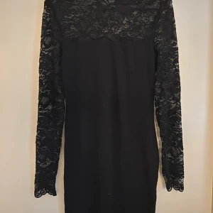 Svart klänning med spetsdetaljer - Säljer en elegant svart klänning med vackra spetsdetaljer på ärmarna och överdelen. Klänningen är långärmad och perfekt för en festlig kväll😍