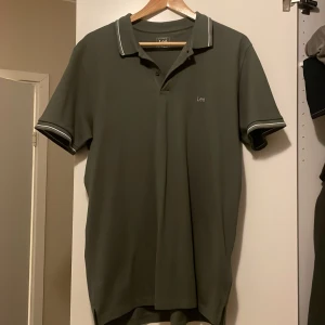 Olivgrön pikétröja från Lee - Säljer en snygg olivgrön pikétröja från Lee i storlek L. Tröjan har korta ärmar och en klassisk krage med vita detaljer. Perfekt för både vardag och lite mer uppklädda tillfällen. Den är aldrig använd!