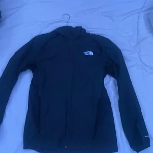 Svart vindjacka från The North Face - Säljer en svart vindjacka från The North Face i mycket bra skick. Jackan har en dragkedja framtill och är långärmad. Perfekt för höst och vår när det blåser lite extra. Den är använd ett fåtal gånger och har inga hål eller något sånt