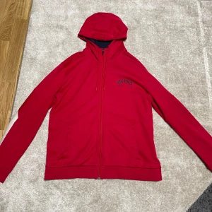 Röd huvtröja från Hugo Boss - Säljer en snygg röd huvtröja från Hugo Boss i storlek L. Tröjan har en dragkedja framtill och en broderad logga på bröstet. Perfekt för höst och vår, med en skön passform och långa ärmar. Materialet känns mjukt och bekvämt. Passar både till vardags och lite mer avslappnade tillfällen. 🌟