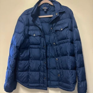 Blå quiltad jacka från Polo Ralph Lauren - Säljer en snygg blå quiltad jacka från Polo Ralph Lauren i storlek XL. Jackan har långa ärmar och praktiska fickor med knappar. Perfekt för höst och vinter, med en stilren look och bekväm passform. Passar både till vardags och lite finare tillfällen. 🧥💙