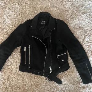 Svart skinnjacka från Zara - Snygg svart mockajacka från Zara i mycket bra skick. Den har en asymmetrisk dragkedja och flera fickor med dragkedjor. Jackan har ett bälte i midjan, nypris ca 400