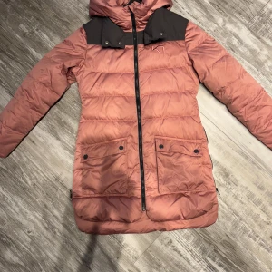 Rosa dunjacka från Kari Traa - Säljer en snygg rosa dunjacka från Kari Traa i storlek S. Jackan har en dragkedja framtill och praktiska fickor med knappar. Den är perfekt för kalla dagar med sin varma vaddering och har en cool kontrastdetalj i mörkare färg på axlarna. Perfekt för höst och vinter!