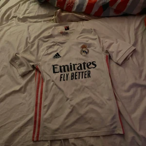 Vit Real Madrid fotbollströja från Adidas 164/XS/S - Säljer en vit Real Madrid fotbollströja från Adidas i storlek 164. Tröjan har korta ärmar och är i mycket bra skick. Den har klubbens emblem och sponsorlogga på framsidan. Perfekt för alla fotbollsfans! ⚽Tröjan passar XS och S väldigt bra också👍