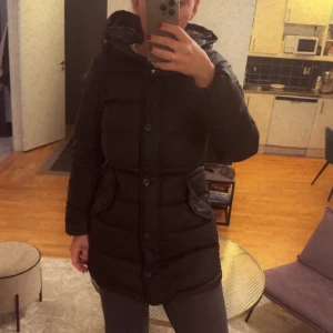 Svart dunjacka GANT  - Svart dunjacka från Gant i mycket bra skick. Den har en skön huva och praktiska fickor framtill. Jackan är perfekt för kalla vinterdagar och har en snygg, figurnära passform. Stängs med knappar och dragkedja för extra värme. Perfekt för både vardag och vinteräventyr! Lite liten för mig så bilderna gör den inte helt rättvisa. Uppskattar en snabb affär så pris kan diskuteras. Nypris 5999 kr 