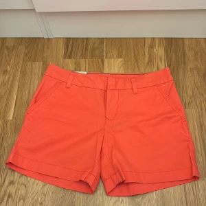 Korallfärgade shorts från Tommy Hilfiger - Snygga korallfärgade shorts från Tommy Hilfiger i 100% bomull. De har en klassisk design med fickor fram och bak, samt hällor för bälte. Perfekta för sommardagar och avslappnade tillfällen. 🧡