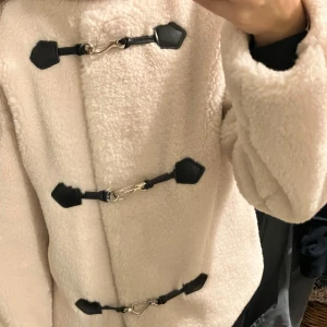 Beige/ vit teddyjacka med svarta detaljer - Säljer denna populära supermysiga beige/ vita teddyjackan med svarta spännen framtill. Perfekt för höst och vinter när du vill hålla dig varm och stilren. 