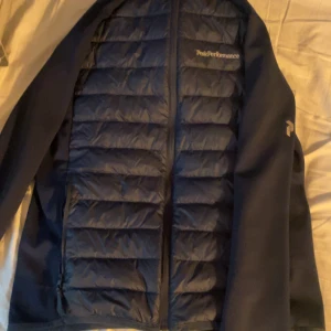 Blå jacka från Peak Performance - Säljer en snygg blå jacka från Peak Performance. Den har en quiltad design med dragkedja och långa ärmar. Perfekt för höst och vår, och den är i mycket bra skick. Jackan är både stilren och funktionell, idealisk för vardagsbruk eller lättare utomhusaktiviteter. Aldrig använt någonsin. Det är storlek M