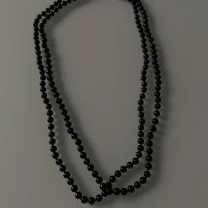 Svart pärlhalsband - Snyggt svart pärlhalsband som passar perfekt till både vardag och fest. Halsbandet är långt och kan bäras i flera lager för en trendig look. Pärlorna är jämna och glänsande, vilket ger en elegant touch till vilken outfit som helst.