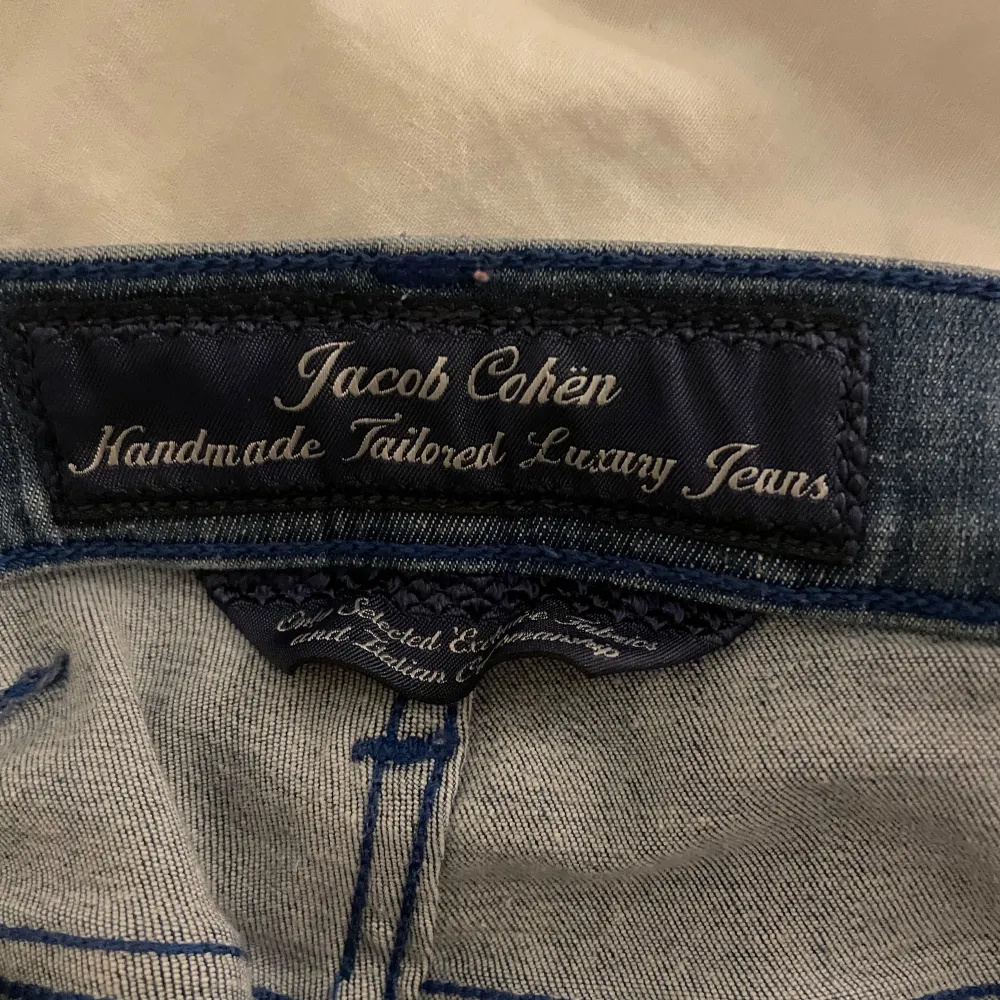 Säljer ett par snygga blå jeans från Jacob Cohën. De är handgjorda och har en lyxig känsla. Jeansen har en tight passform och är perfekta för både vardag och fest. Märkesdetaljer finns på baksidan och insidan av midjan. Passar perfekt för dig som vill ha stil och komfort i ett!. Jeans & Byxor.