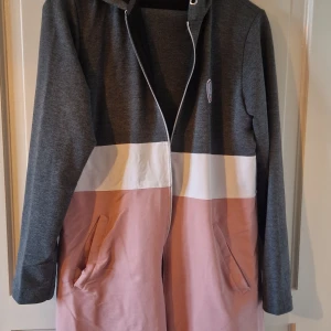 Grå och rosa långärmad pyjamas från Elf Olive - Säljer en snygg och bekväm pyjamas från Elf Olive i storlek XL. Den har en cool färgblockdesign i grått, vitt och rosa. Jackan är långärmad med dragkedja och har praktiska fickor framtill. Perfekt för höst och vår!