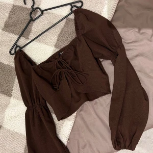 Hm blus topp, S - En brun topp med långa ärmar och en knytning i mitten. Toppen är cropped och har en lös passform. Storlek s.