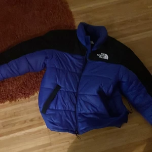 Blå och svart pufferjacka från The North Face - Säljer en snygg blå och svart pufferjacka från The North Face i storlek L. Jackan har en dragkedja framtill och är perfekt för kalla dagar. Den är i mycket bra skick och har långa ärmar. Perfekt för vintern eller hösten! ❄️