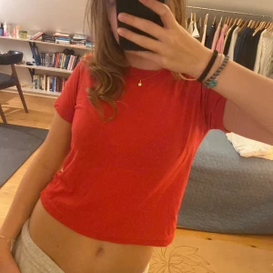 Röd croppad t-shirt - Säljer en snygg röd croppad t-shirt i bra skick. Perfekt för sommardagar eller som en basplagg i garderoben. Den har en enkel design med korta ärmar och en bekväm passform.