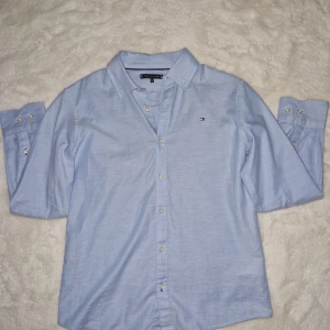  Tommy Hilfiger skjorta - Säljer en ny ljusblå skjorta från Tommy Hilfiger. Använd ett fåtal gånger. Storleken står 152 fast den passar 162 och XXS