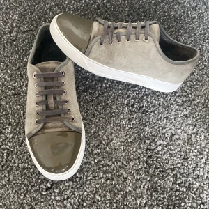 Lanvin skor - Säljer ett par grå sneakers i mocka med en cool lackad tådel. De har snörning och en vit sula som ger en snygg kontrast. Perfekta för både vardag och fest! 🕺Mycket bra skick, enda lilla defekt är lite missfärgning vid skosnören men går säkert att lösa och syns inte vid användning av skorna!