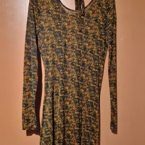 Mönstrad klänning från Dagmar - Säljer en superfin mönstrad klänning från Dagmar i storlek S. Klänningen har ett färgglatt mönster i gult, orange och svart. Den har långa ärmar och en snygg öppen rygg med drapering. Perfekt för höst och vår! 🖤💛