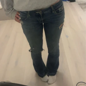 Blå jeans med slitningar - Säljer ett par snygga blå jeans med slitningar på knäna. Har sytt ut dem själv där nere