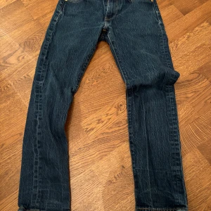 Levi's 502 jeans med broderad detalj - Säljer ett par sällsynta Levi's 502 jeans i mörkblå denim. De har en cool gul broderad kanin på bakfickan och klassisk röd Levi's etikett. Jeansen är i bra skick och har en straight/slim passform. De släpptes bara under 2021/2022. De gör inte såna här byxor längre. 