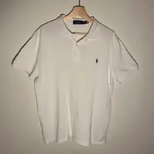 Säljer en klassisk vit pikétröja från Polo Ralph Lauren i storlek M. Tröjan har korta ärmar och den ikoniska loggan broderad på bröstet. Perfekt för en stilren och avslappnad look. Passar både till vardags och festliga tillfällen.