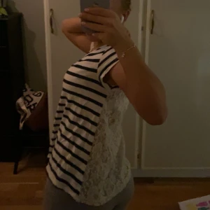 Randig topp med spetsdetaljer - Säljer en superfin randig topp med spetsdetaljer på ryggen. Den är kortärmad och har en avslappnad passform, perfekt för vardagar. Toppen är i mycket bra skick och passar både till vardags och lite finare tillfällen.