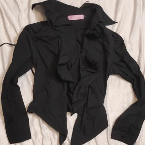 Svart blus med volangdetaljer Lolita/vampyr inspirerad  - Snygg svart blus med volangdetaljer och knappar framtill. Perfekt för en festlig kväll eller en stilren vardagslook. Blusen har långa ärmar och en elegant krage som ger en chic touch. Passar bra till både jeans och kjol! Lolita/vampyr inspirerad med en kortsett på ryggen