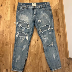 Blå slitna jeans från ONE TEASPOON  - Säljer ett par blå jeans från ONE TEASPOON i bra skick. De har en cool, sliten look med flera revor och slitningar på framsidan. Jeansen har en normal passform och är perfekta för en avslappnad stil, ”Mom jeans”. Dragkedjor vid bensluten ger en extra edge. Perfekta för höst och vår! Storlek 30/32 skulle jag säga, men går till anklarna. 