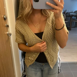 Kortärmad kofta - En superfin beige stickad kofta med lite guldglittriga detaljer i tyget. I bra skick. Storlek M men passar mig som brukar ha xs/s