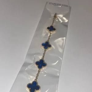 Armband i rostfritt stål med blå klöver - Snyggt armband i rostfritt stål med fem blå klöverformade hängen. Perfekt för att ge en färgklick till din outfit. Armbandet har en elegant kedja och är lätt att matcha med andra smycken. Passar både till vardags och fest!
