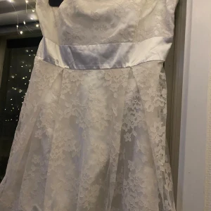 Vit spetsklänning från Vila - Säljer en elegant vit klänning från Vila i storlek XL. Klänningen har ett vackert spetsmönster och en satinliknande midja som ger en fin kontrast. Perfekt för festliga tillfällen!