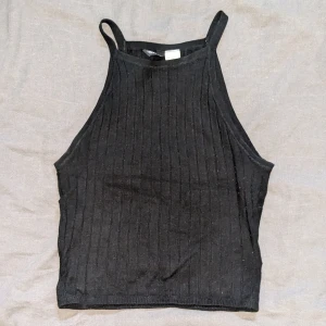 Svart ribbad linnetopp från Divided - Säljer en snygg svart ribbad linnetopp från h&m. Den är ärmlös med smala axelband och har en tight passform. Perfekt för sommardagar eller som ett lager under en jacka.