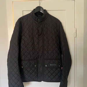 Svart quiltad jacka från Belstaff - Säljer en snygg svart quiltad jacka från Belstaff. Jackan har en stilren design med långa ärmar och praktiska fickor framtill. Den är perfekt för höst och vår, och har både dragkedja och knappar för stängning. Jackan är i nyskick och redo för nya äventyr!