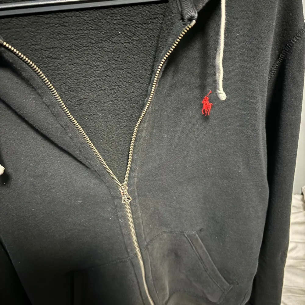 Säljer en snygg svart hoodie från Polo Ralph Lauren i storlek M. Den har en dragkedja framtill och en klassisk röd logga på bröstet. Hoodien har långa ärmar och en justerbar huva med vita snören. Perfekt för höst och vinter!. Tröjor & Koftor.