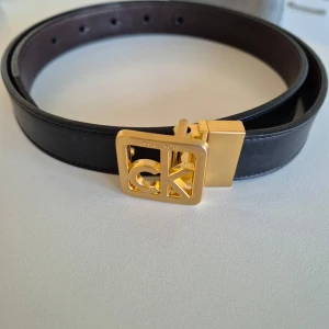 Bälte Calvin Klein - Bälte från märket Calvin Klein. Knappt använd. Läder. Guld märke och svart bälte. 