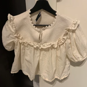 Vit blus med volangdetaljer - Säljer en superfin vit blus med volangdetaljer runt halsen och ärmslut. Perfekt för vår och sommar!