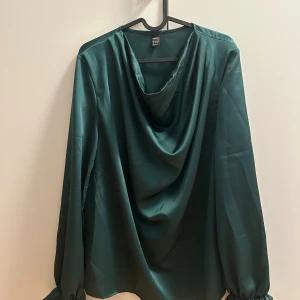 Draperad hals - smaragdgrön blus - Mycket fin smaragdgrön blus med lite drapering i halsen och volang på ärmarna  Aldrig använd   Bild 2 är mest lik färg i verkligheten, mörkare grön