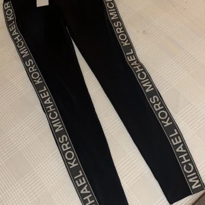 Svarta leggings från Michael Kors - Säljer ett par snygga svarta leggings från Michael Kors i storlek XS. De har en stilren design med Michael Kors-loggan längs sidorna. Perfekta för både vardag och fest!